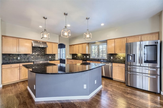 kitchen featuring a kitchen island, appliances with stainless steel finishes, pendant lighting, and wall chimney range hood