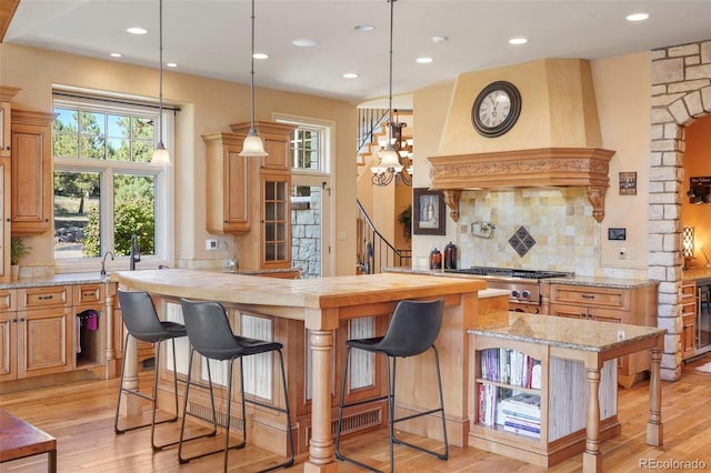 1975 Fox Mountain Pt, Colorado Springs, CO 80906 - kitchen featuring light wood finished floors, tasteful backsplash, a kitchen bar, hanging light fixtures, and custom exhaust hood