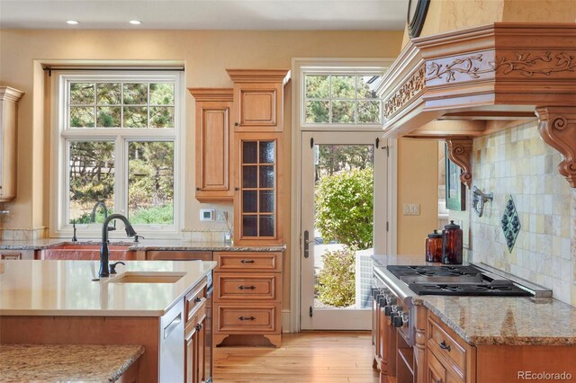 1975 Fox Mountain Pt, Colorado Springs, CO 80906 - kitchen with brown cabinets, premium range hood, tasteful backsplash, a sink, and light wood-style floors