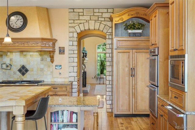 1975 Fox Mountain Pt, Colorado Springs, CO 80906 - kitchen featuring a warming drawer, tasteful backsplash, stainless steel appliances, arched walkways, and light wood-style floors