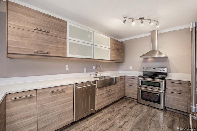 kitchen with dark wood-style floors, appliances with stainless steel finishes, a sink, wall chimney range hood, and modern cabinets