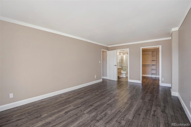 unfurnished bedroom with crown molding, a walk in closet, dark wood finished floors, and baseboards