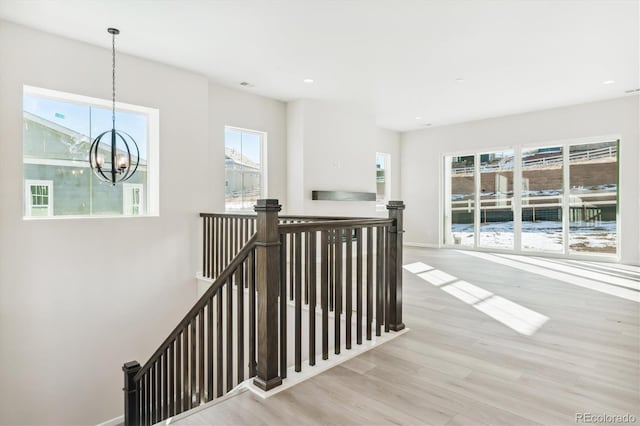 stairs with a healthy amount of sunlight, a notable chandelier, and hardwood / wood-style flooring