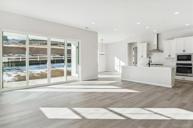 kitchen with oven, wall chimney range hood, light wood-type flooring, built in microwave, and white cabinetry