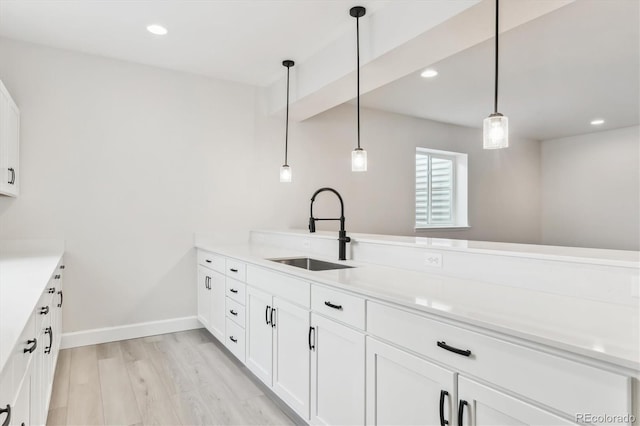 kitchen featuring pendant lighting, light hardwood / wood-style floors, white cabinets, and sink