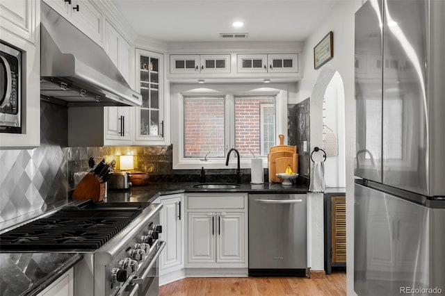 1265 S Elizabeth St, Denver, CO 80210 - kitchen featuring appliances with stainless steel finishes, under cabinet range hood, white cabinetry, dark stone countertops, and glass insert cabinets