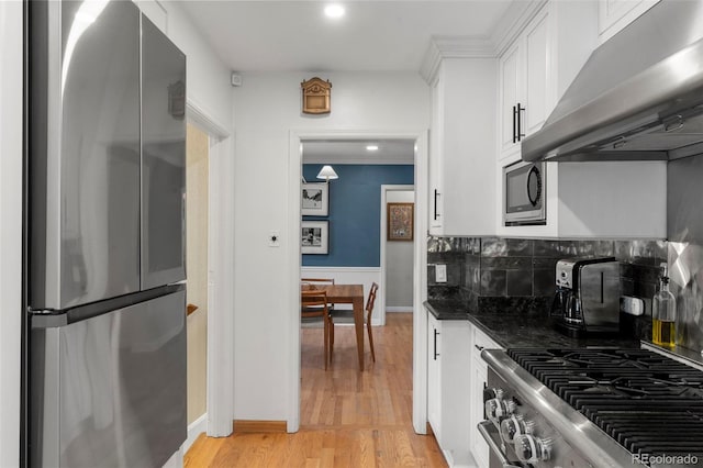 1265 S Elizabeth St, Denver, CO 80210 - kitchen with appliances with stainless steel finishes, exhaust hood, white cabinetry, tasteful backsplash, and light wood-style floors