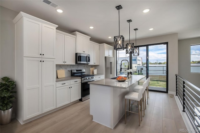 kitchen featuring light wood-type flooring, visible vents, a center island with sink, backsplash, and appliances with stainless steel finishes