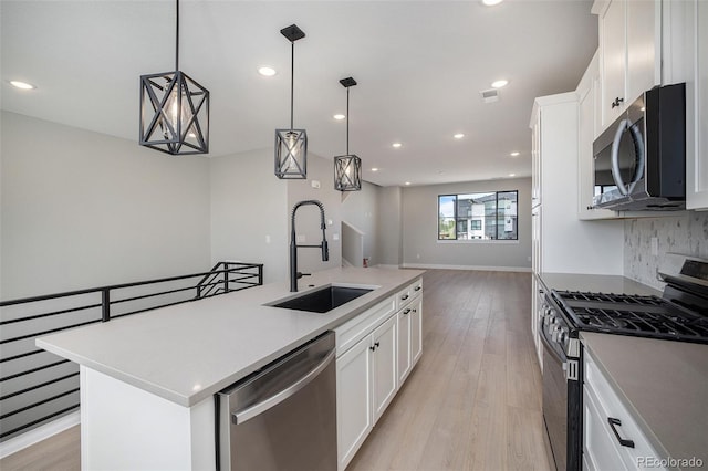 kitchen with a kitchen island with sink, a sink, light wood-style floors, appliances with stainless steel finishes, and open floor plan