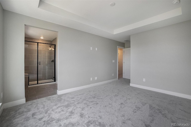 unfurnished bedroom with ensuite bath, a raised ceiling, carpet flooring, and baseboards