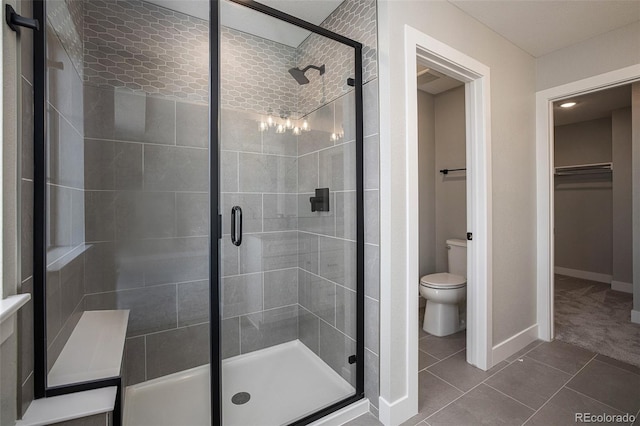 full bath featuring a stall shower, toilet, a walk in closet, and baseboards