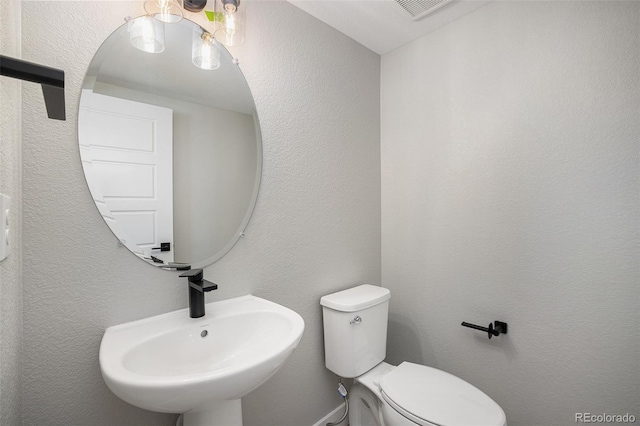 half bathroom featuring visible vents, toilet, a textured wall, and a sink