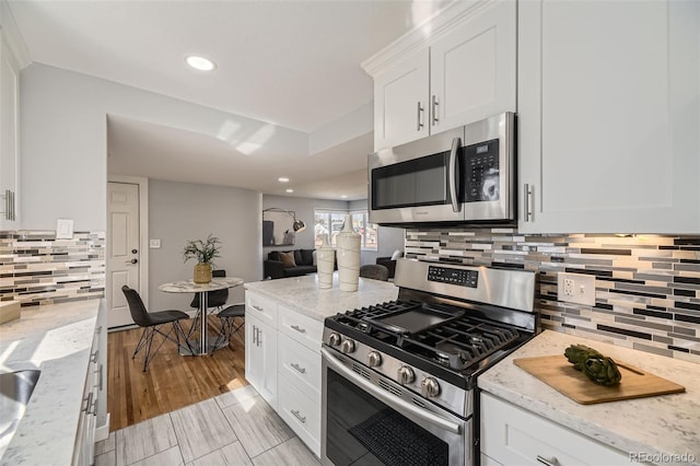 kitchen with white cabinets, light stone countertops, stainless steel appliances, and backsplash