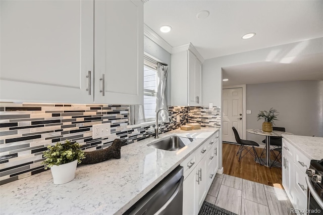 kitchen with stainless steel appliances, a sink, white cabinetry, backsplash, and light stone countertops