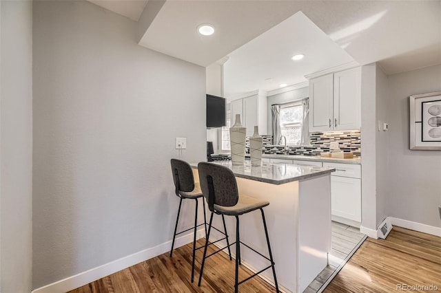 kitchen featuring tasteful backsplash, white cabinets, a peninsula, light wood-style floors, and a kitchen bar