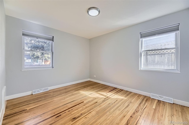 empty room with light wood-type flooring, visible vents, and baseboards