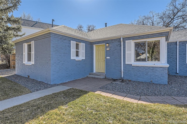 view of front of property with entry steps, brick siding, a front lawn, and a shingled roof