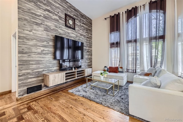 living room featuring visible vents, an accent wall, wood finished floors, and plenty of natural light