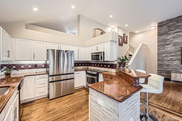 kitchen with a breakfast bar area, a peninsula, dark stone counters, and stainless steel appliances