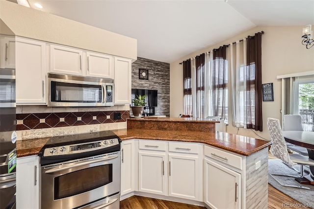 kitchen featuring white cabinetry, tasteful backsplash, appliances with stainless steel finishes, a peninsula, and dark stone countertops