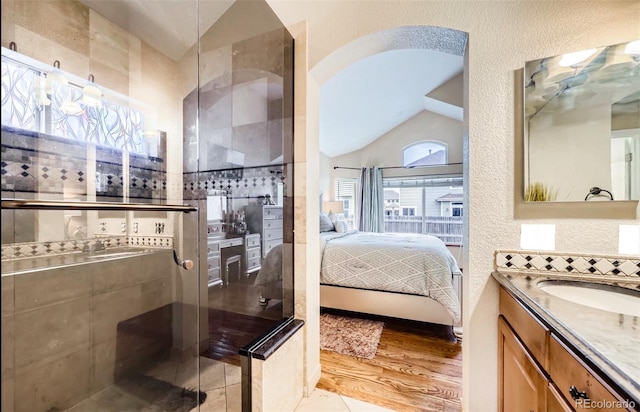bathroom featuring ensuite bath, lofted ceiling, a textured wall, and vanity