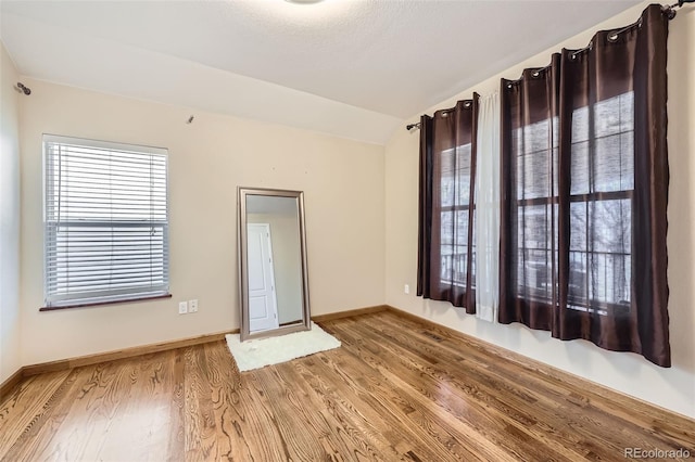 spare room featuring baseboards, lofted ceiling, and wood finished floors