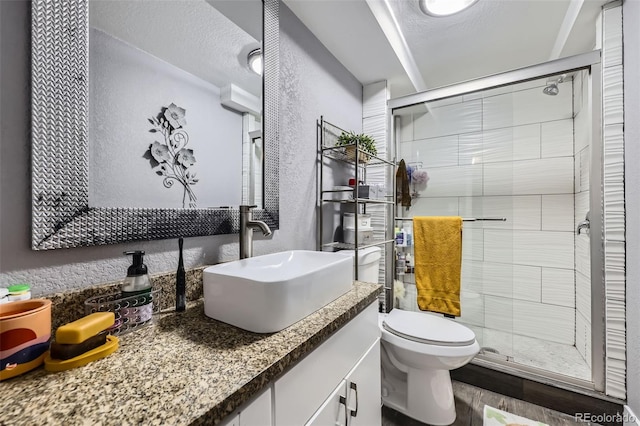 full bathroom with a stall shower, toilet, vanity, a textured ceiling, and a textured wall