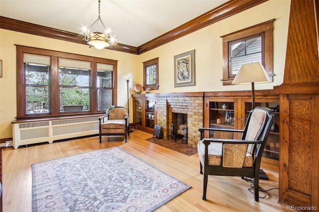 sitting room featuring radiator heating unit, ornamental molding, a brick fireplace, and an inviting chandelier