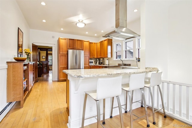 kitchen featuring brown cabinetry, freestanding refrigerator, a peninsula, island range hood, and a healthy amount of sunlight