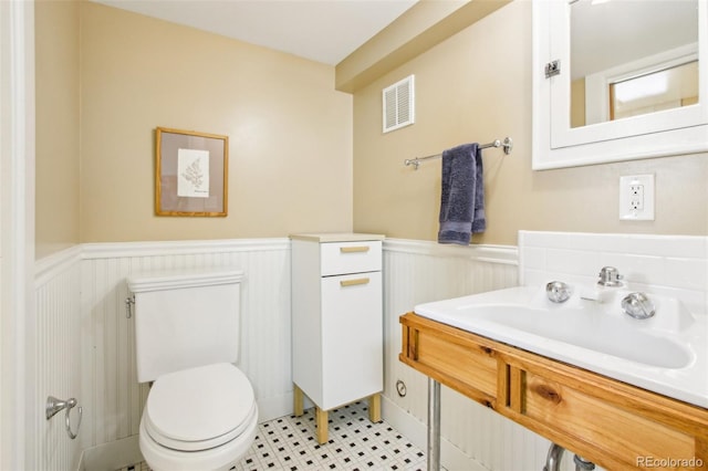 half bathroom with visible vents, a sink, a wainscoted wall, and toilet
