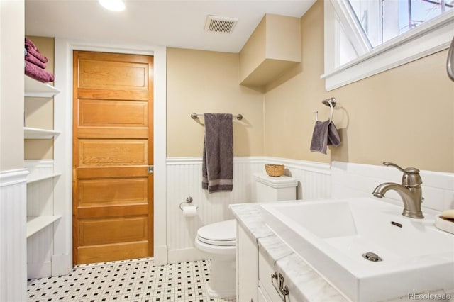 bathroom featuring vanity, toilet, visible vents, and a wainscoted wall