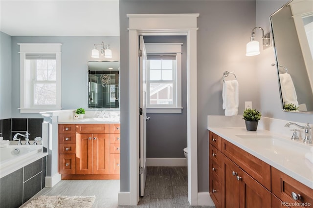 bathroom with plenty of natural light, a relaxing tiled tub, toilet, and vanity