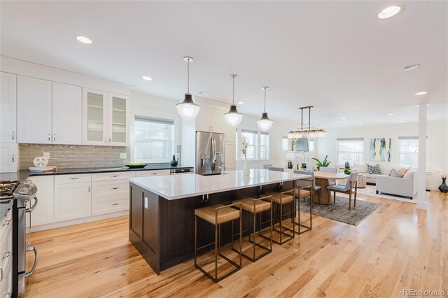 kitchen featuring a breakfast bar, a center island with sink, decorative backsplash, appliances with stainless steel finishes, and white cabinetry