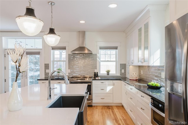 kitchen featuring tasteful backsplash, white cabinetry, wall chimney range hood, and appliances with stainless steel finishes