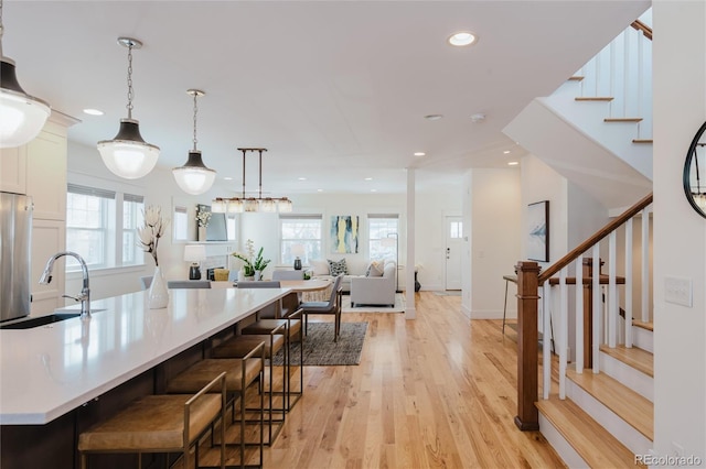 kitchen with pendant lighting, a large island with sink, a kitchen breakfast bar, sink, and light hardwood / wood-style floors