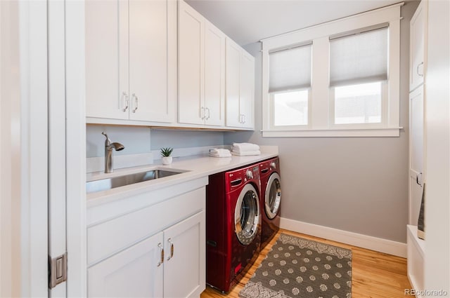 clothes washing area with light hardwood / wood-style floors, cabinets, separate washer and dryer, and sink