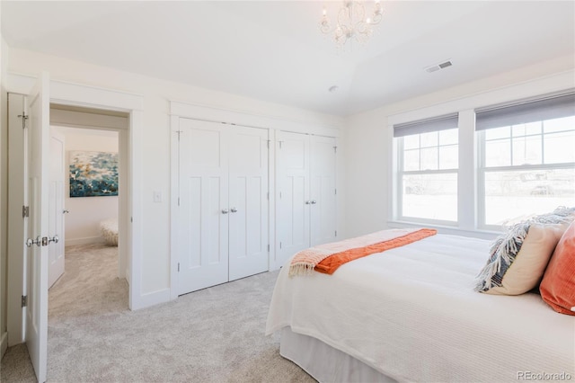 bedroom featuring light carpet, a chandelier, and two closets