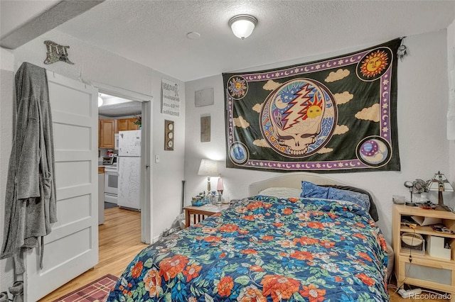 bedroom with light hardwood / wood-style floors, white fridge, and a textured ceiling