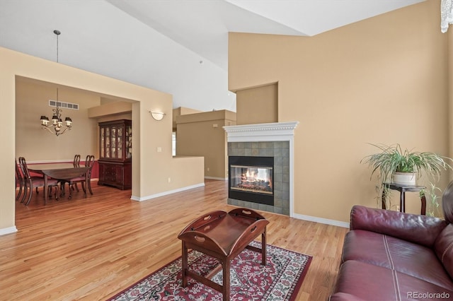 living area with a fireplace, visible vents, an inviting chandelier, vaulted ceiling, and light wood-type flooring