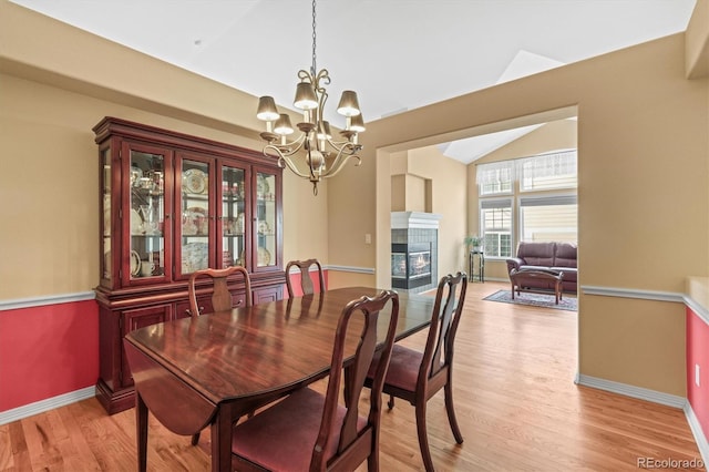 dining room with a tile fireplace, light wood-style flooring, a notable chandelier, baseboards, and vaulted ceiling