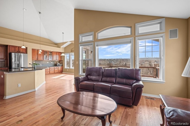 living room featuring light wood-style floors, baseboards, visible vents, and high vaulted ceiling