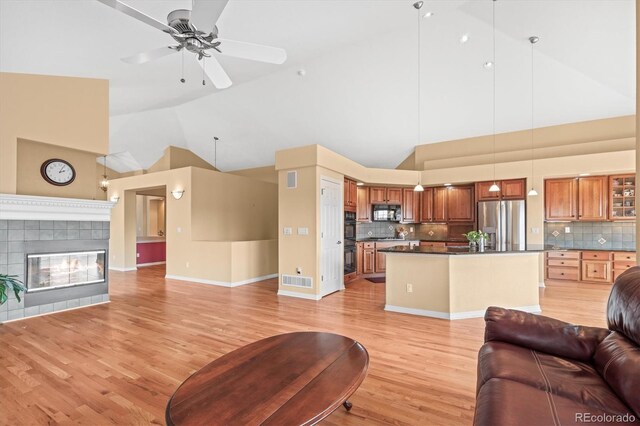 living room with visible vents, light wood-style floors, ceiling fan, high vaulted ceiling, and a tile fireplace