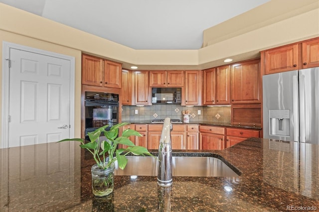 kitchen with a sink, backsplash, dark stone counters, black appliances, and brown cabinetry