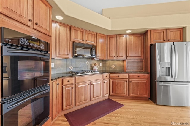 kitchen with light wood-style flooring, brown cabinets, backsplash, and black appliances