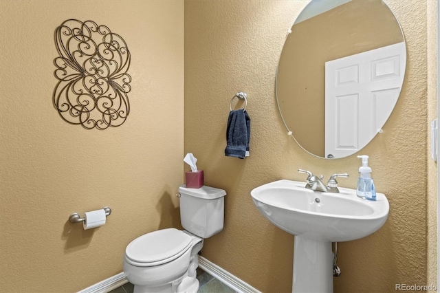 bathroom featuring baseboards, a textured wall, and toilet