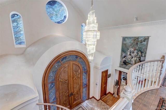 entryway with a chandelier, high vaulted ceiling, ornamental molding, and wood finished floors