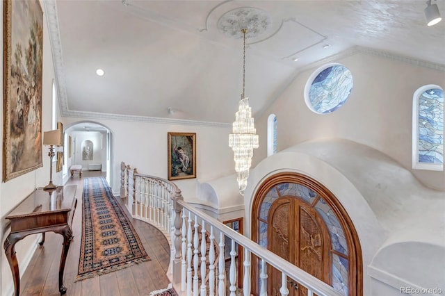 hall with arched walkways, a chandelier, an upstairs landing, vaulted ceiling, and wood-type flooring