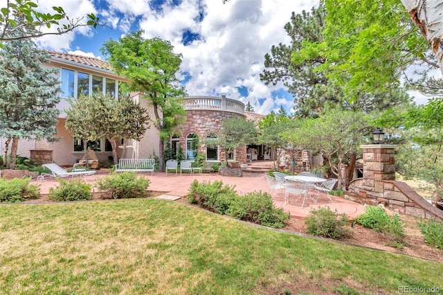 rear view of house with a patio, a yard, stone siding, and stucco siding