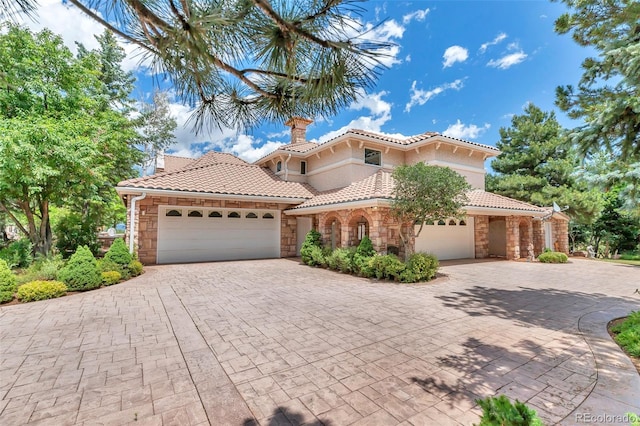 mediterranean / spanish-style house with decorative driveway, stone siding, a tiled roof, and a garage