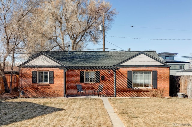 view of front facade featuring a shingled roof, a front yard, fence, and brick siding